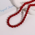 Vue détaillée de perles rouges brillantes de 10mm sur une assiette en céramique blanche - 1 Pièce / Rouge