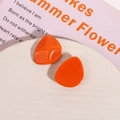 Close-up of orange irregular resin earrings on a white tray with pink book backdrop - Orange