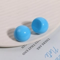 Close-up of bright blue glossy spherical resin beads on white ceramic tray for DIY jewelry - Blue