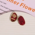 Detailed macro view of asymmetric burgundy resin earrings with gold rose relief texture - Gold Rose