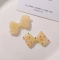 Detailed view of resin bow clips in solid cream and colorful polka dot pattern on a tray - Beige