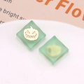 Detail view of square translucent green resin Halloween charms with gold pumpkin face designs - Green