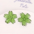 Macro shot of two translucent green cherry blossom resin charms on a white ceramic tray - Green