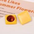 Close-up of yellow resin square earrings with amber-patterned round inlay on white stand - Yellow