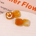 Detail of amber resin square charms with marble texture and white smiley face pattern - Brown
