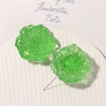 Dettaglio macro di un ciondolo a forma di margherita in resina verde su piatto bianco - Verde