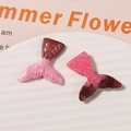 Close-up of glitter mermaid tail resin charms for DIY jewelry on a textured white plate - Red
