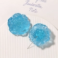 Macro shot of icy blue resin flower charms with textured petals and metal pin base - Blue