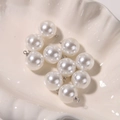 Close-up of polished white round pearl pendants with silver metal loops in a shell bowl - 14mm