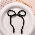 Handmade black beaded bow hair clip accessory displayed on a white ceramic plate - Black