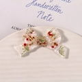 Macro shot of resin bow pendant with dried flowers and white pearl on a ceramic tray - White