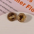 Close-up of asymmetric resin earrings with woven straw fiber inlay on ceramic dish - Yellow Coffee