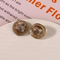 Macro shot of retro amber resin stud earrings with gold woven edge on a white tray - Gray