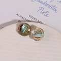 Close-up of vintage resin earrings with gold metal rim and marbled texture on ceramic tray - Green