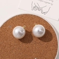 Close-up of two white faux pearl pendants with gold metal loops on a cork coaster - 20mm