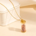 Close-up of golden cylinder glass pendant filled with brown stones on white leather box - Red Stone Style (0838)