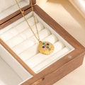 Dettaglio di collana dorata con pendente rotondo e pietre colorate su velluto bianco - Stile Croce Strass Colorata Ovale (0873)