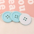 Vista macro di bottoni rotondi a 4 fori blu pastello e bianchi per accessori moda - Blu
