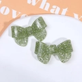 Macro detail of grass green glitter bow hair clip on an oval white ceramic tray - Green