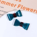 Detail of dark teal acetate bow hair clips with red accents on a white plate - Blue