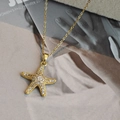 Collier pendentif étoile de mer dorée avec cristaux sur fond de magazine de mode - Étoile de Mer Pavée Dorée (EXRGN0412JS)