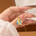 Handheld shot of a gold tropical fish necklace with blue and yellow enamel pendant details - Blue Fish
