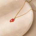 Detailed close-up of a gold necklace with a red Christmas glove pendant on ceramic plate - Heart Christmas Glove Necklace