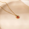 Detail view of gold Christmas bell enamel pendant on a ceramic plate with silk fabric - Bell Round Plate Pendant Necklace