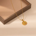 Detail of gold circular zodiac pendant necklace with stars and stones on a display box - Aries