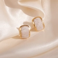 Vue macro de boucles d'oreilles dorées avec texture marbrée sur tissu en soie - Pierre Blanche Géométrique Clou (1847)