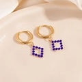 Vue détaillée de créoles dorées avec zircon bleu sur un fond de satin chaleureux - Boucles d'Oreilles Zirconia Bleu Losange Creux