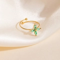 Détail d'une bague ajustable dorée ornée d'un trèfle en zircon vert sur tissu en soie - Style Fleur en Croix Verte