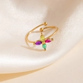 Détail d'une bague dorée avec zircons colorés posée sur un tissu de soie blanche douce - Style Fleur de Croix Multicolore