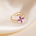 Gros plan d'une bague trèfle dorée avec zircons violets sur soie beige - Style Fleur de Croix Violette