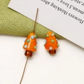 Detailed macro of handmade orange mushroom glass beads with blue dots for jewelry making - Orange