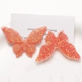 Macro shot of two butterfly resin charms with pink glitter for DIY hair accessories - Orange