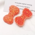 Macro detail of sparkly resin bow charms with glitter sequins for DIY crafts and accessories - Orange
