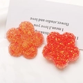 Makroaufnahme von orange-roten Glitzer-Blumenanhängern aus Harz für DIY-Schmuck - Orange