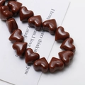 Macro view of glossy caramel ceramic heart beads with holes for DIY jewelry making - Dark Coffee