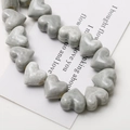 Macro view of heart-shaped grey ceramic beads with marble texture and vertical holes - Gray