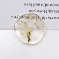 Macro detail of clear oval resin pendant featuring white dried flowers and gold foil flakes - White Dried Flower