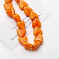Gros plan de perles en céramique orange polies en forme de cœur pour bijoux DIY - Orange