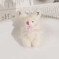 Détail de pendentif lapin en peluche blanche avec étoile argentée et ruban rose sur plat - Beige