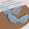 Macro shot of glittery blue resin angel wing charms with layered feather texture - Blue