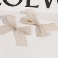 Detail of two champagne mesh bow hair clips on a ceramic tray with elegant textures - Light Coffee