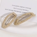 Close-up of cream woven fabric hair clips with gold thread detail on white tray - Light Color