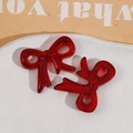 Detail view of two dark red translucent resin bow charms on a white textured ceramic plate - Bow / Dark Red