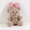 Close-up of curly plush bear with red plaid bow, pearl necklace and heart metal pendant - Brown Bear With Checkered Bow
