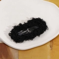Close-up of a black plush BB hair clip with fluffy texture on a white decorative tray - Black