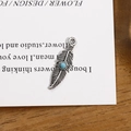 Vue détaillée d'un pendentif plume argentée vintage avec perle turquoise sur bois - Plume d'argent rétro